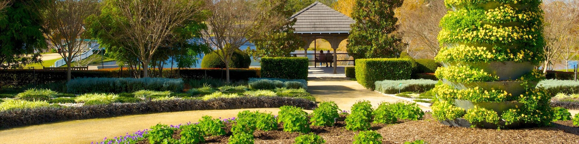 A well-manicured garden with a gazebo, neatly trimmed hedges, and flowering plants.