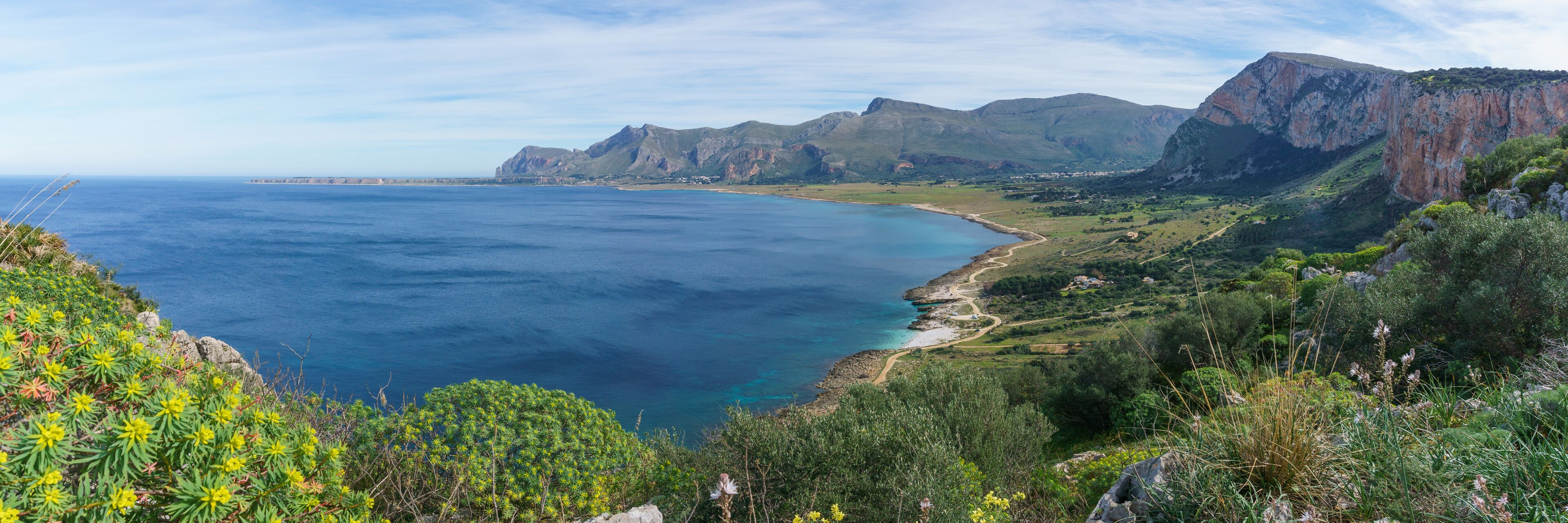 A coastal landscape with cliffs, a beach, and a clear blue sea.