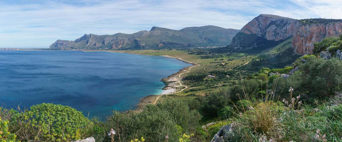 A coastal landscape with cliffs, a beach, and a clear blue sea.
