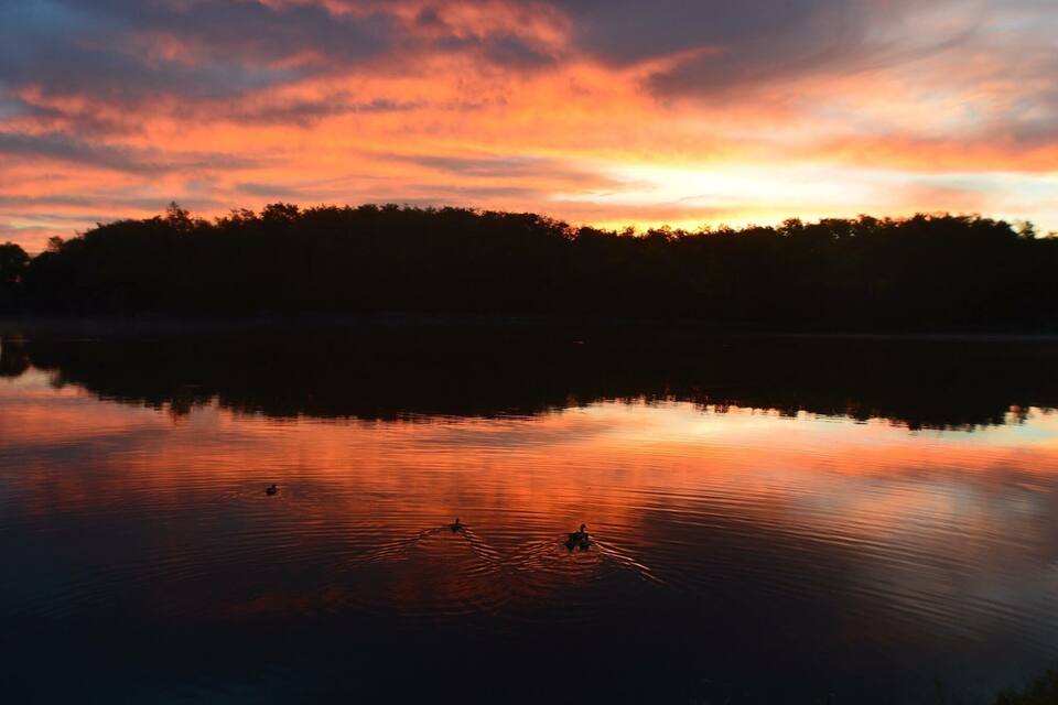 A calm lake at sunset with a forested shoreline and a clear sky.