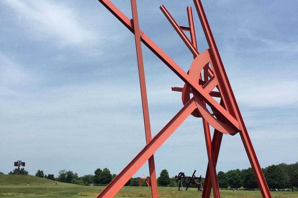 A large red metal sculpture in an open field.