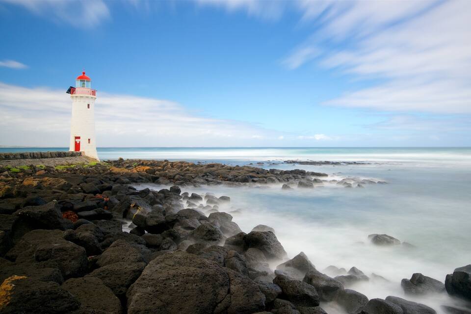Un phare sur une côte rocheuse, sous un ciel dégagé.