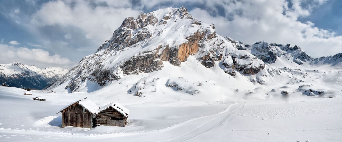 A snow-covered mountain with a wooden cabin in the foreground.