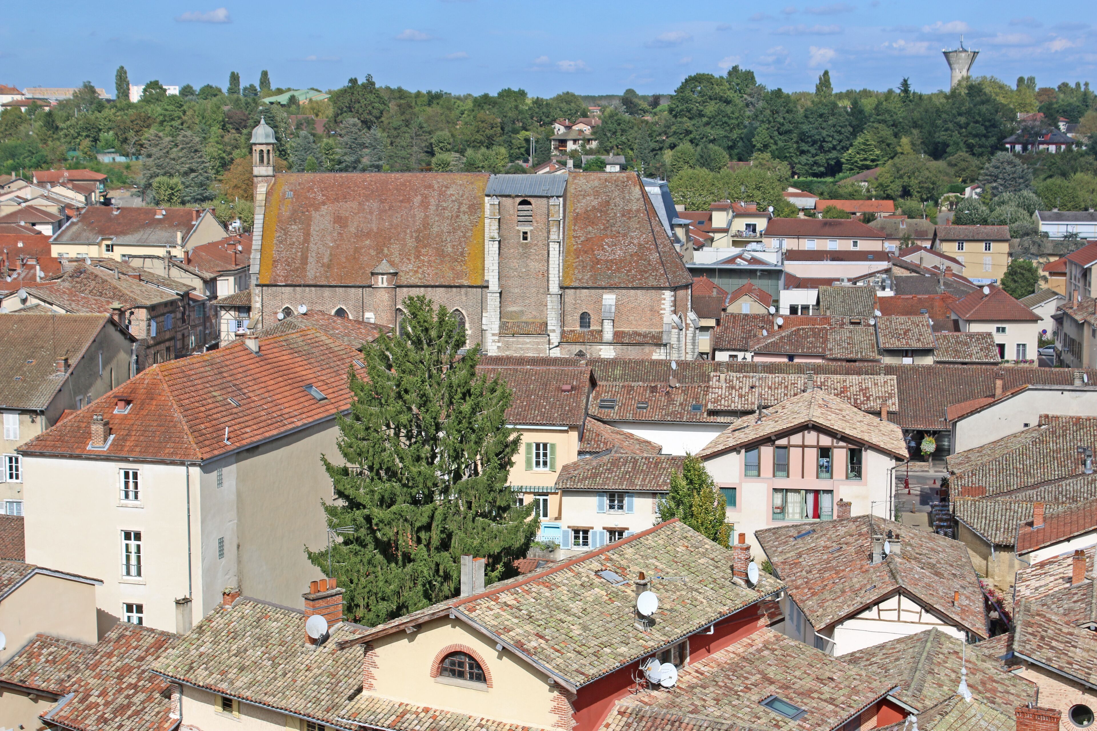A historic town with red-tiled roofs, a prominent church with a bell tower, and lush green hills in the background.