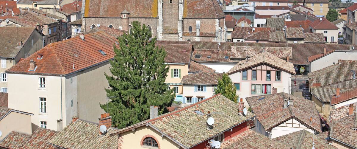 A historic town with red-tiled roofs, a prominent church with a bell tower, and lush green hills in the background.