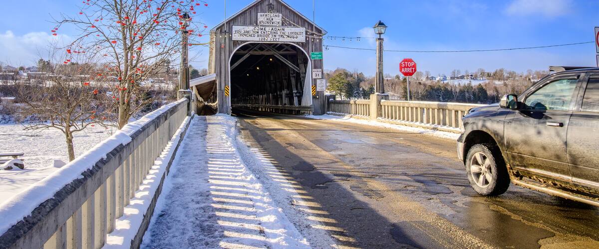 Un pont couvert orné de drapeaux, de la neige sur le sol et une voiture qui approche.