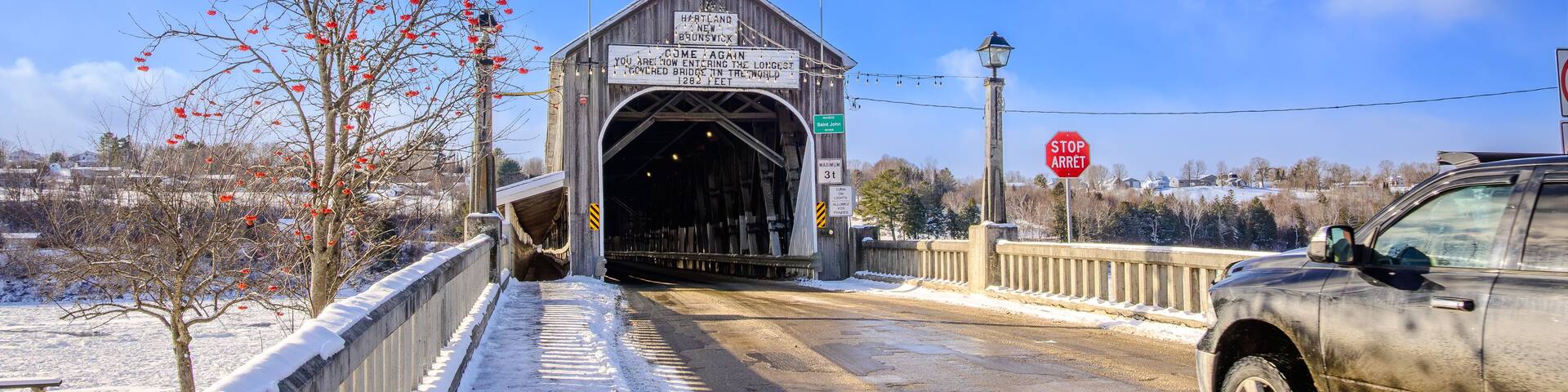 A covered bridge with flags, snow on the ground, and a car approaching.