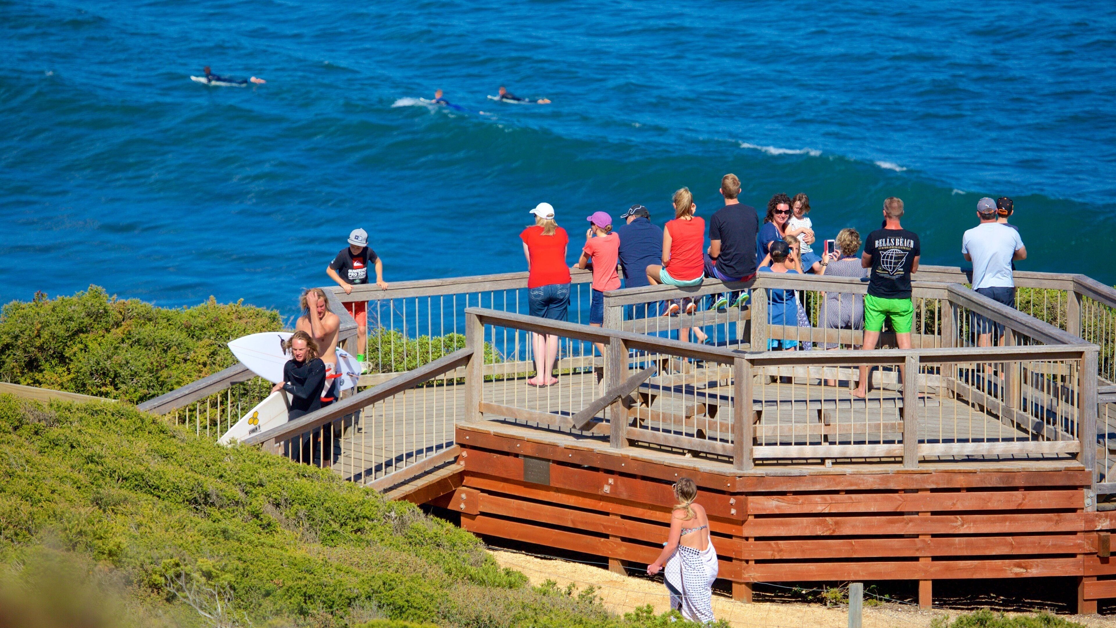 A wooden observation deck overlooking the ocean with people watching surfers.