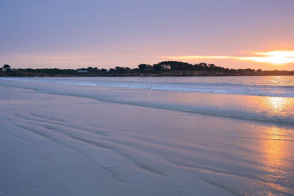 A beach with gentle waves and a sunset over the horizon.