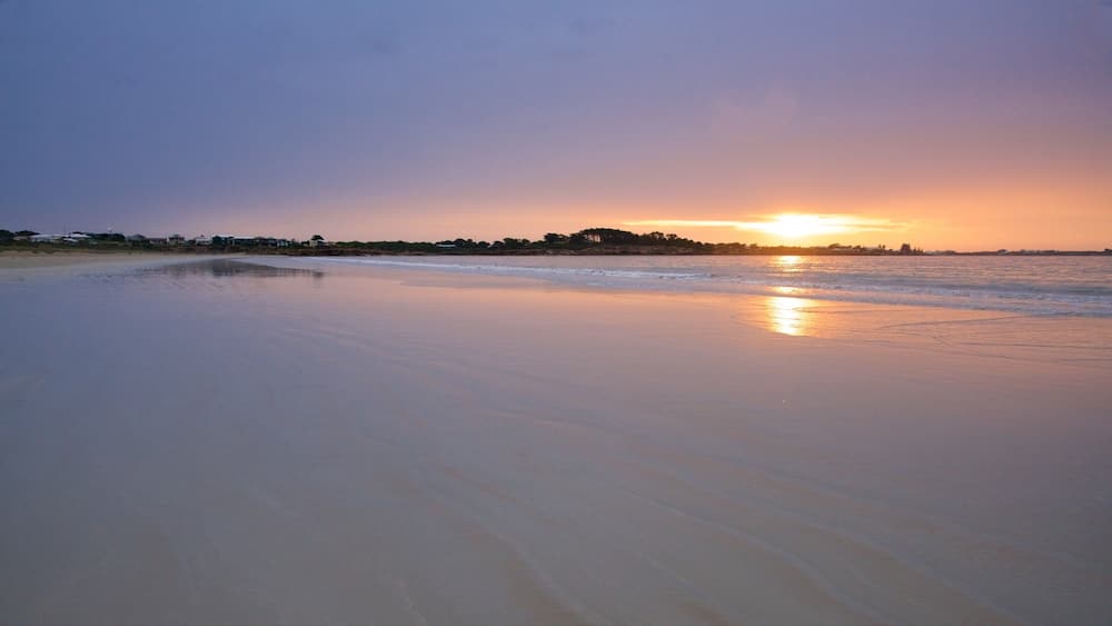 A beach at sunset with calm waters reflecting the sky.