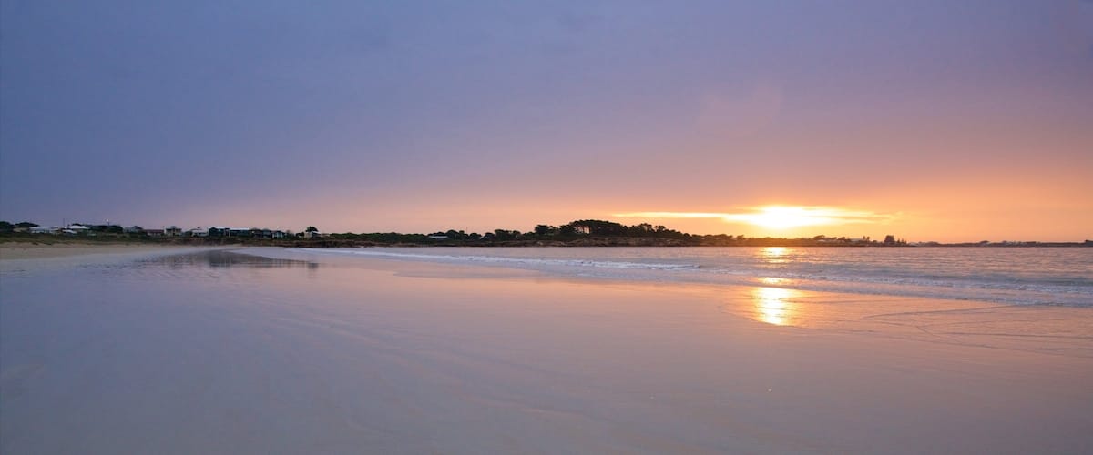 A beach at sunset with calm waters reflecting the sky.