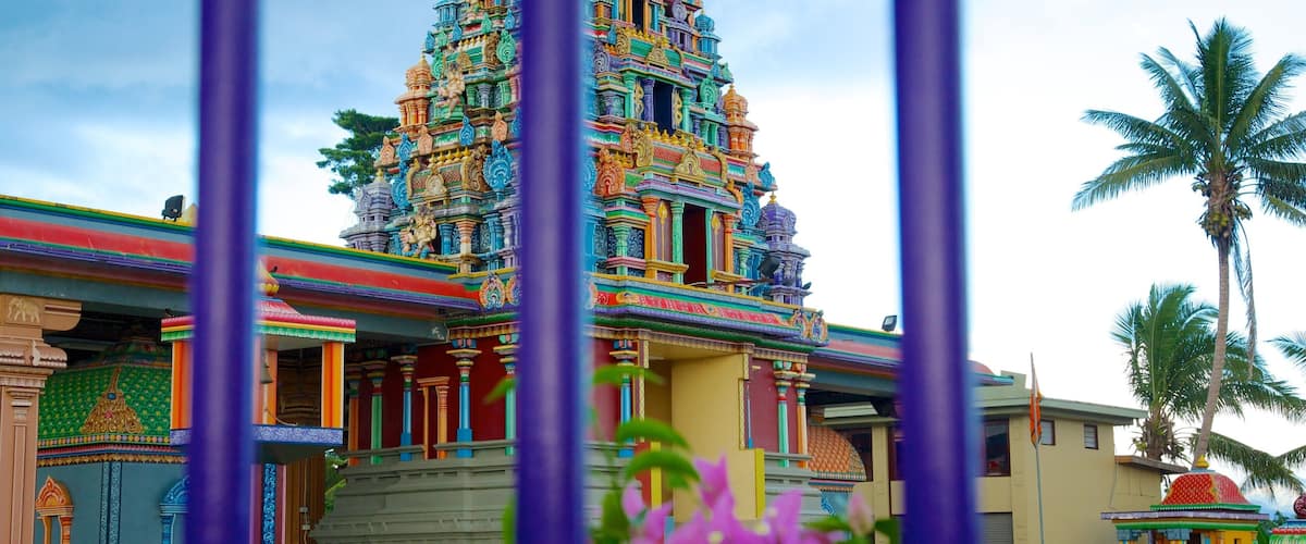 A colorful temple with intricate architecture, a statue in the foreground, and a palm tree in the background.