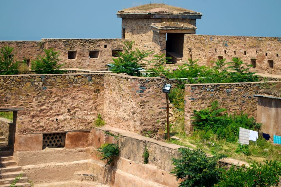 A stone fort with a watchtower, surrounded by greenery and a small staircase.