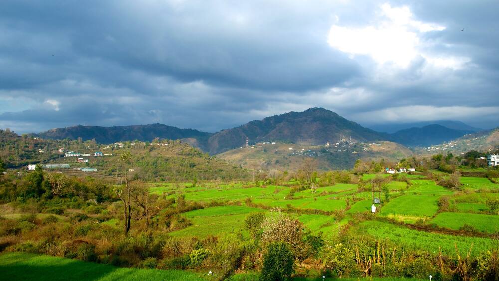 Une vallée verdoyante et luxuriante, avec des champs en terrasses, une chaîne de montagnes lointaine et quelques bâtiments dispersés.