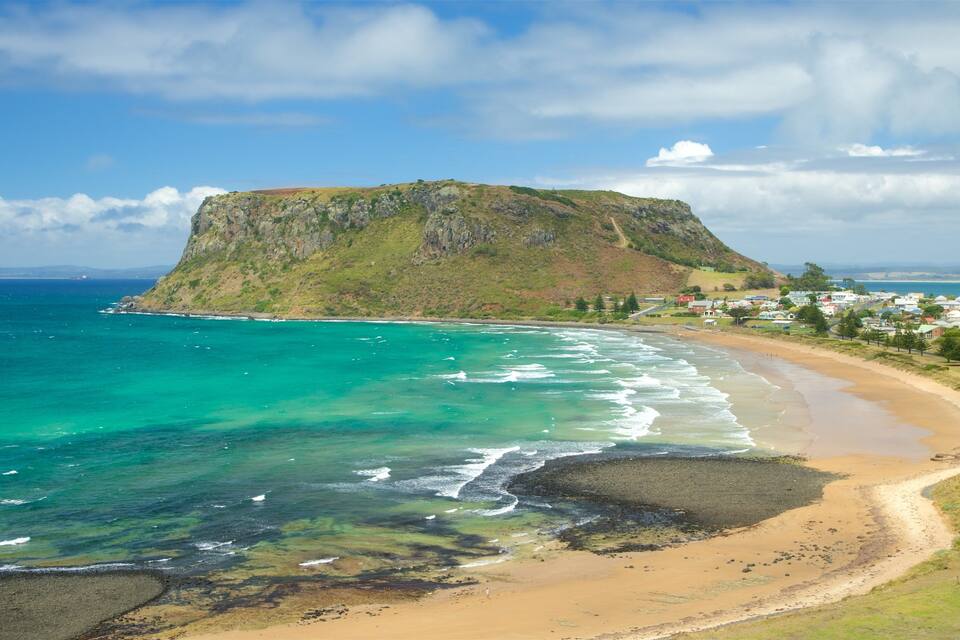 A coastal landscape with a prominent hill, clear turquoise waters, and a sandy beach.