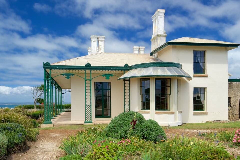 A white house with green accents and a garden with various plants and flowers.