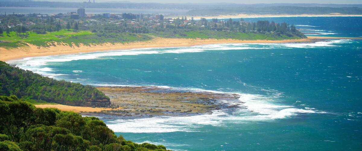 A coastal landscape with a sandy beach, ocean waves, and a distant city skyline.