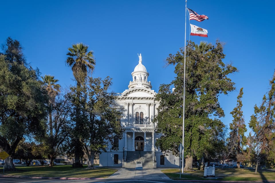 A white capitol building with a dome, surrounded by trees and a clear blue sky.