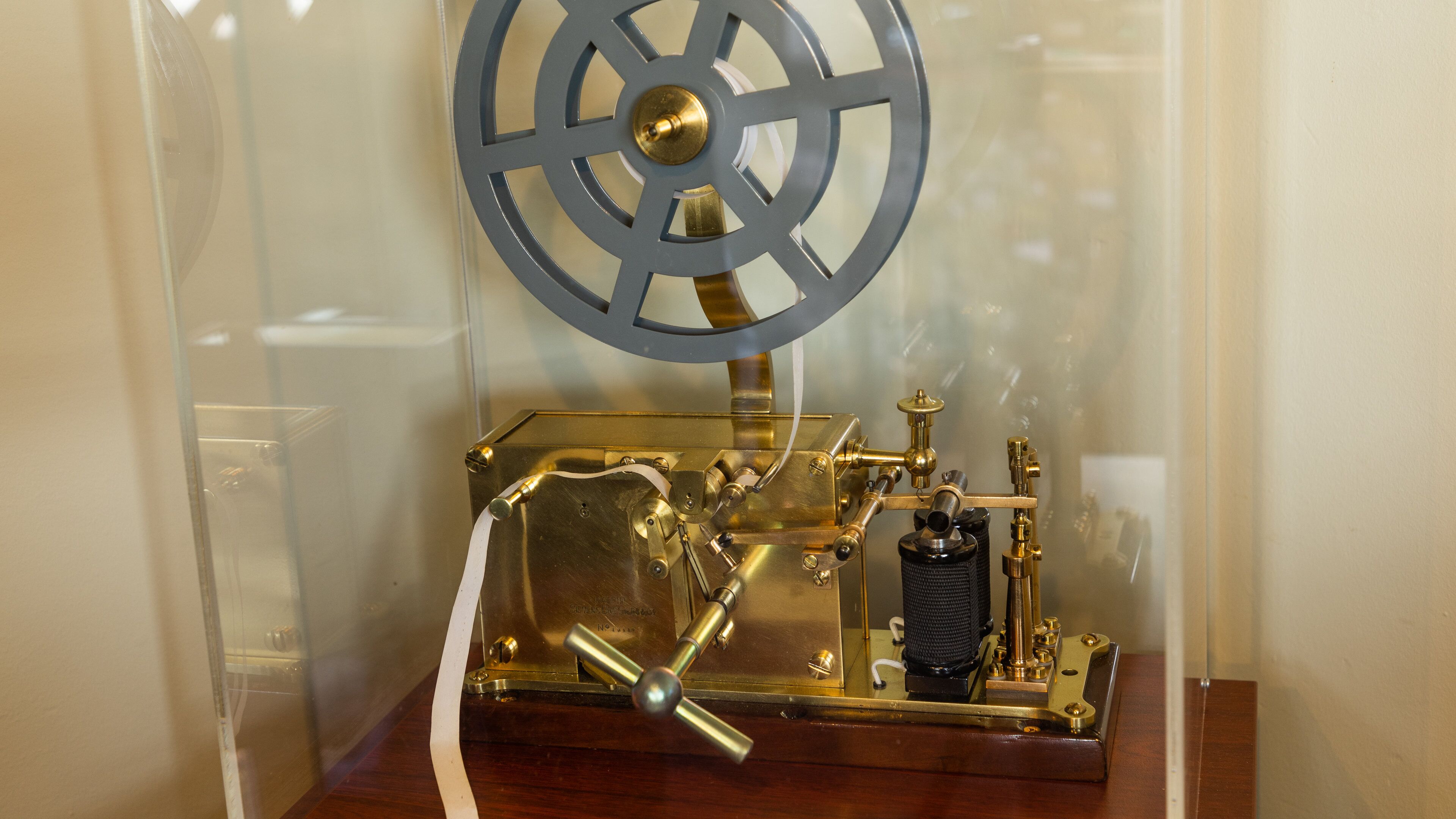 Een messing mechanisch apparaat met een wiel en tandwielen, vermoedelijk een historisch tentoonstellingsobject.