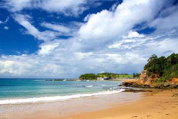 A beach with clear turquoise water, a sandy shore, and a rocky cliff with greenery.