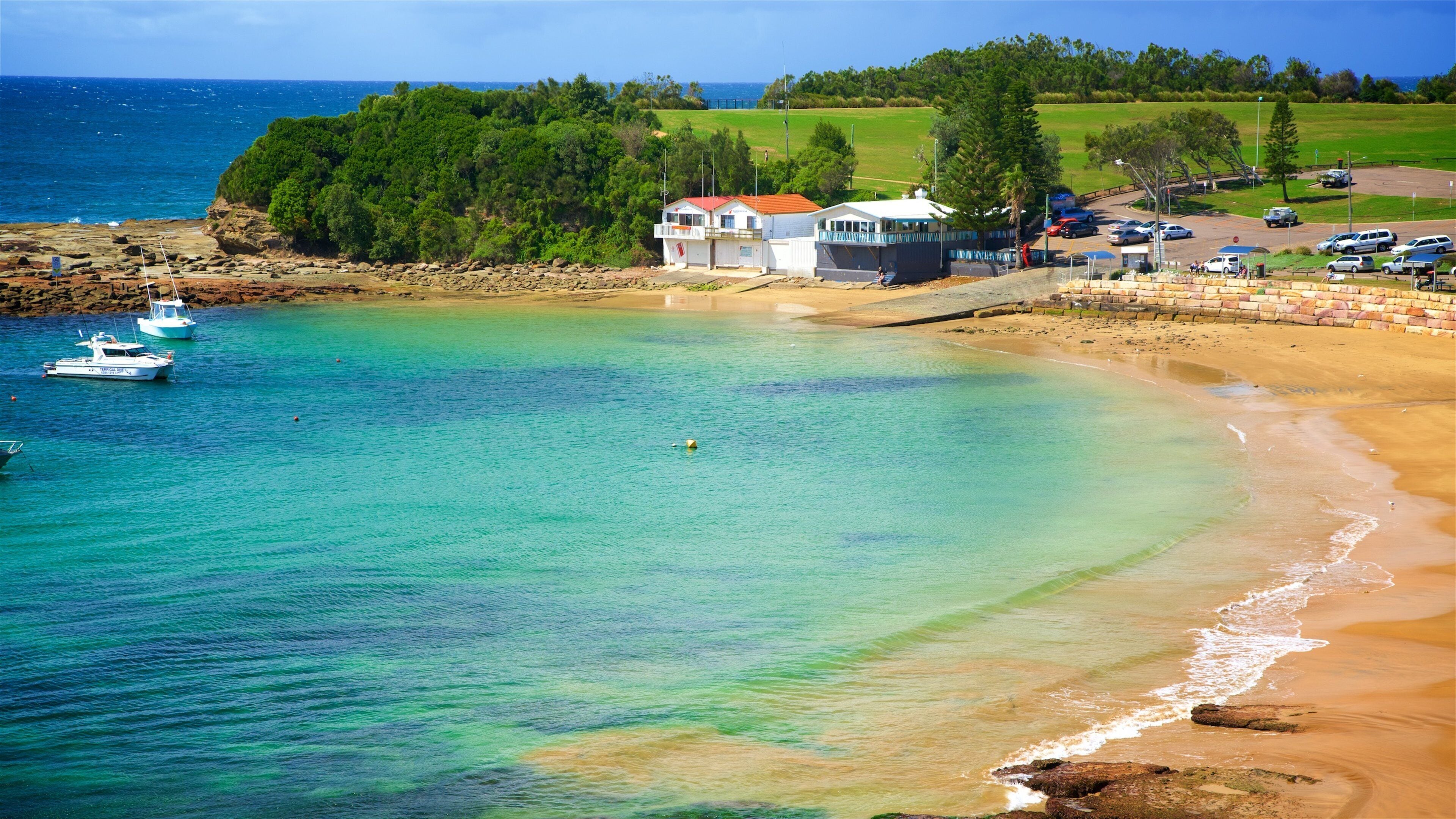A coastal beach with clear turquoise waters, a sandy shore, and a small pier with boats.