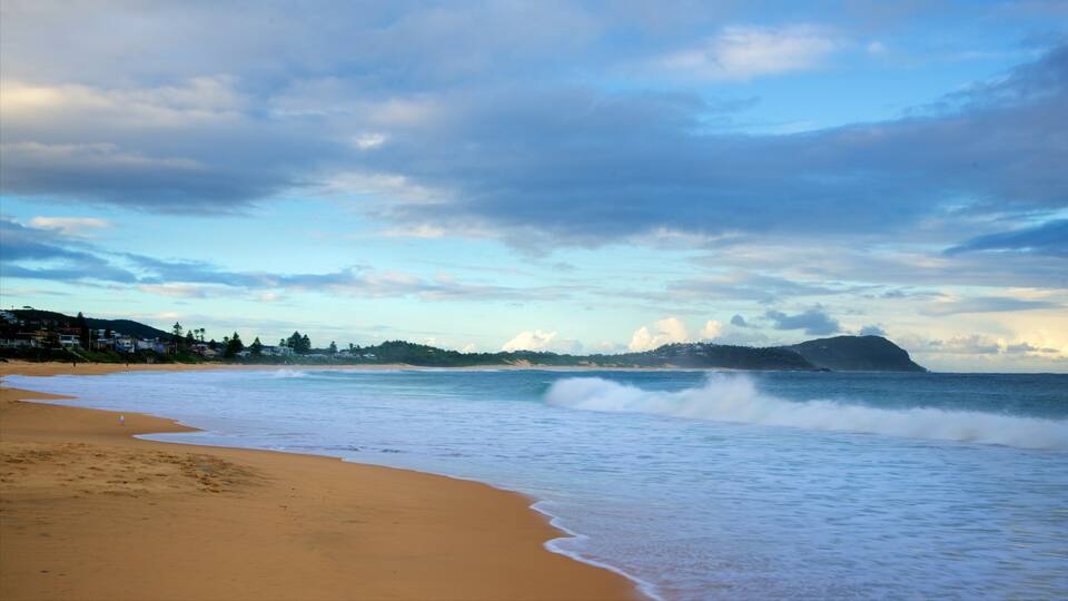 A beach with waves, a distant mountain, and a cloudy sky.