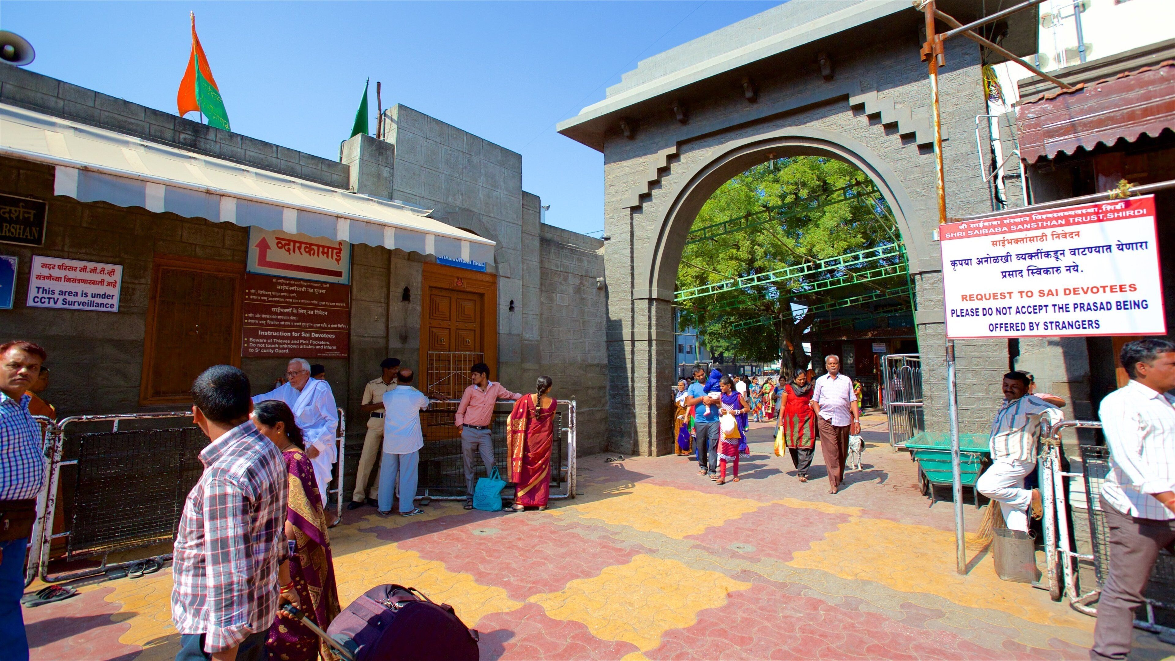 A busy entrance with people, a signboard, and a flag.
