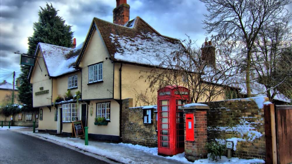 A traditional pub with a red telephone booth and snow on the roof.