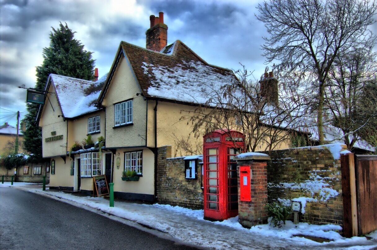 A traditional pub with a red telephone booth and snow on the ground.