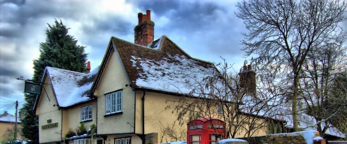 A traditional pub with a red telephone booth and snow on the ground.