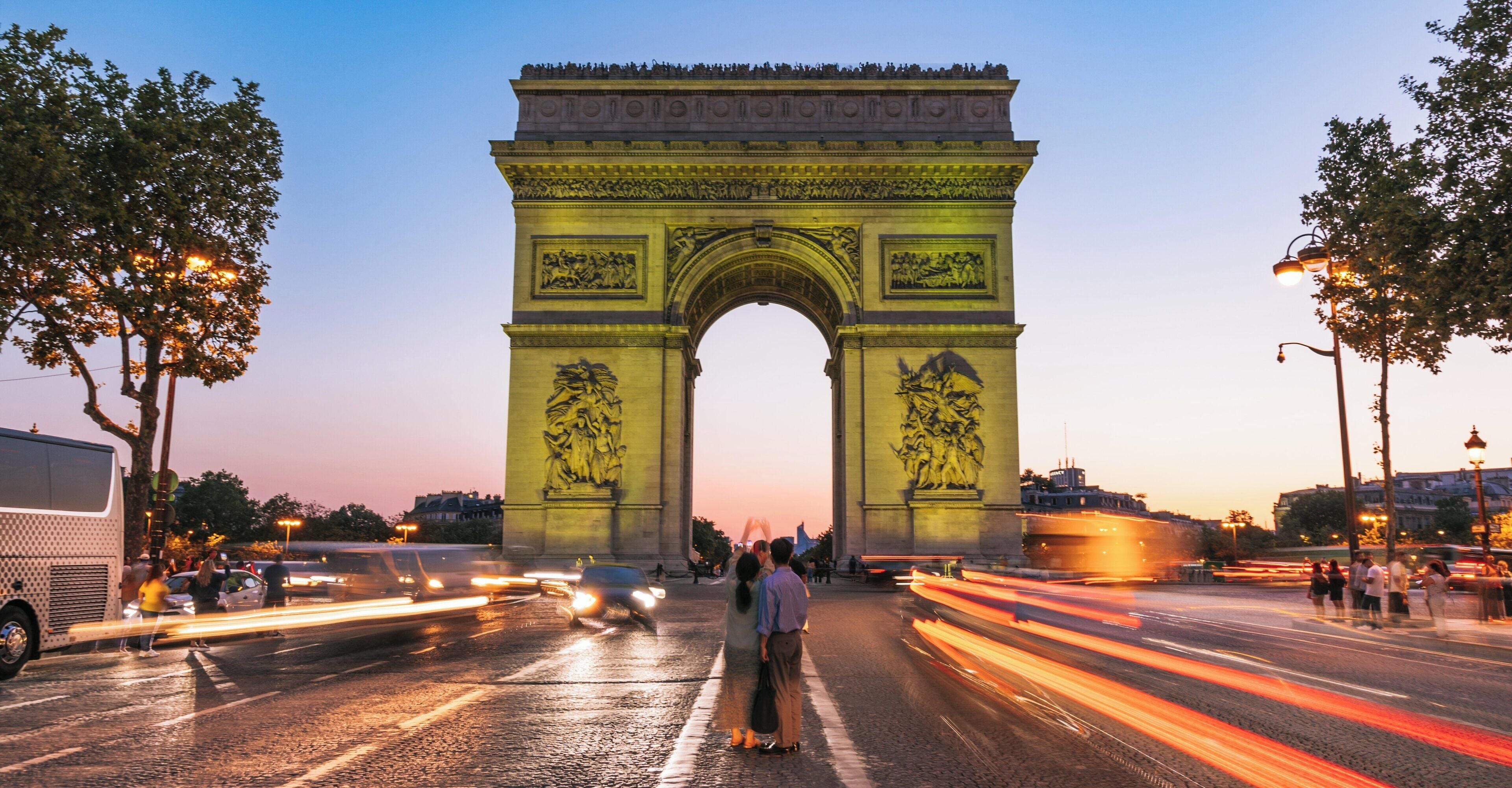 Evening lights illuminate the iconic Arc de Triomphe on Champs-Elysees in Paris, where pedestrians enjoy the vibrant atmosphere of the city