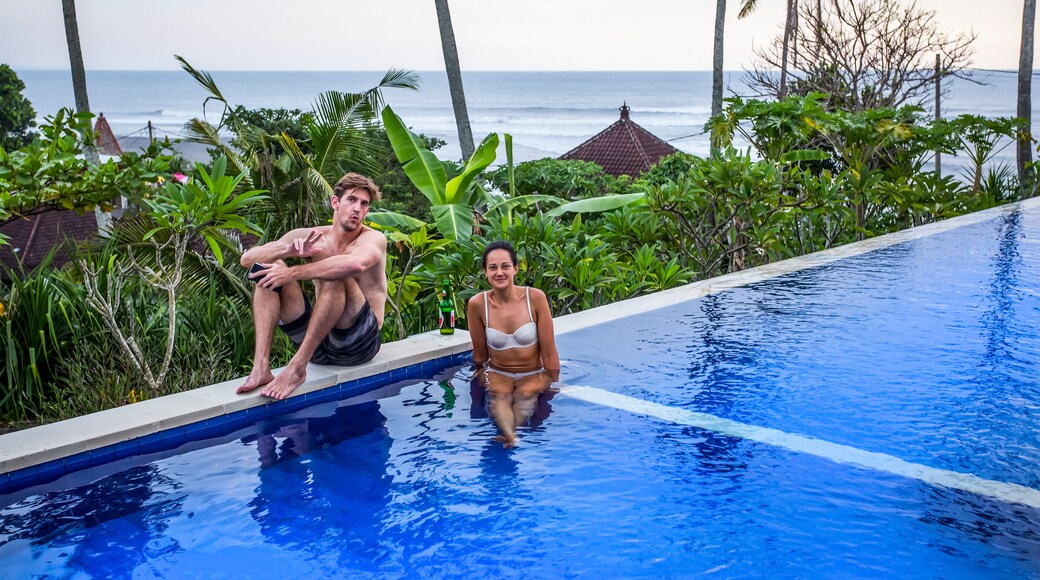 Man and woman sitting poolside at resort, overlooking surfing beach of Balian Beach; Selemadeg Barat, Tabanan, Bali, Indonesia