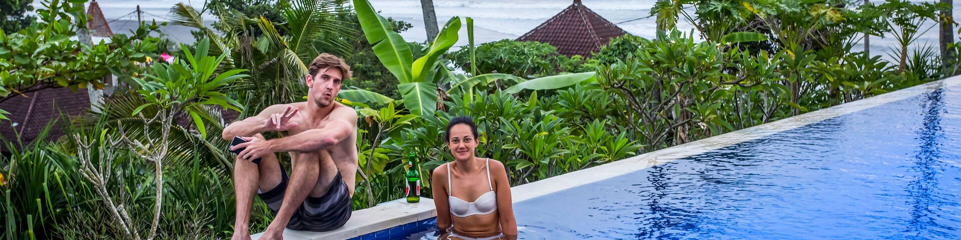 Man and woman sitting poolside at resort, overlooking surfing beach of Balian Beach; Selemadeg Barat, Tabanan, Bali, Indonesia
