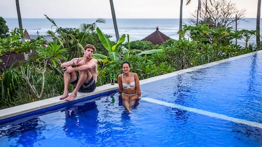 Man and woman sitting poolside at resort, overlooking surfing beach of Balian Beach; Selemadeg Barat, Tabanan, Bali, Indonesia