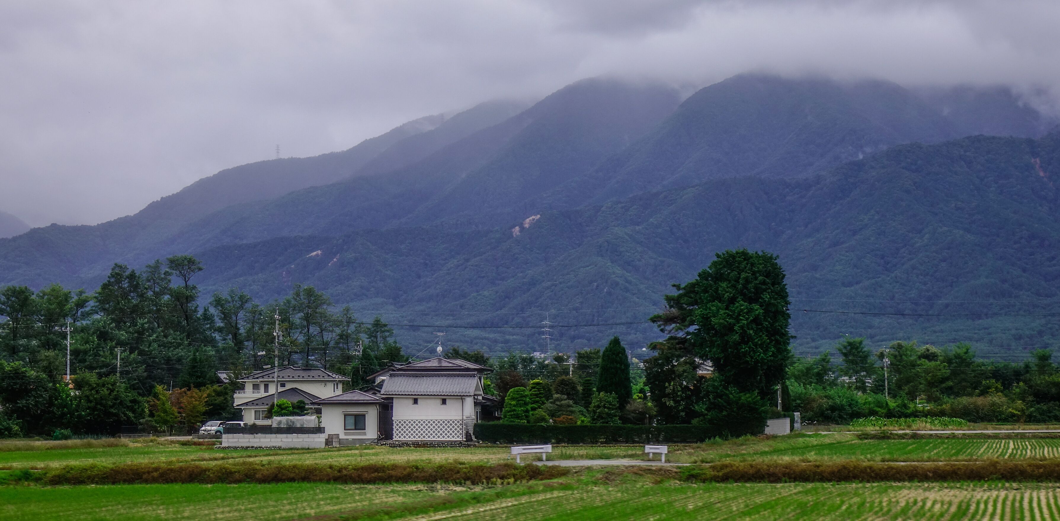 A rural landscape with traditional houses, green fields, and mountains in the background.