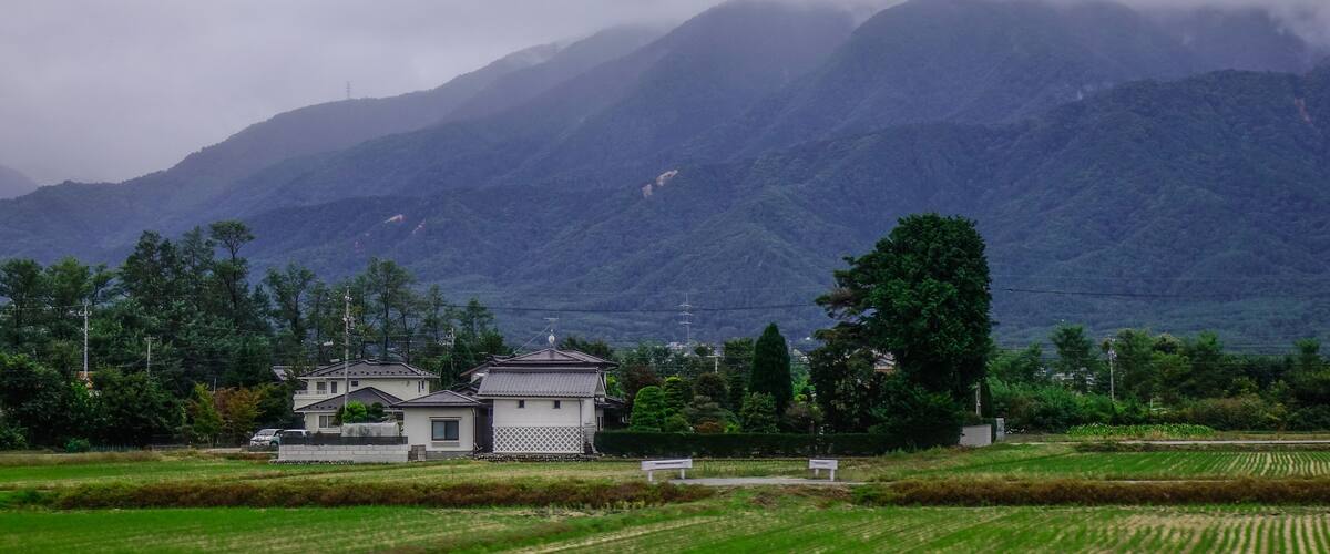 A rural landscape with traditional houses, green fields, and mountains in the background.