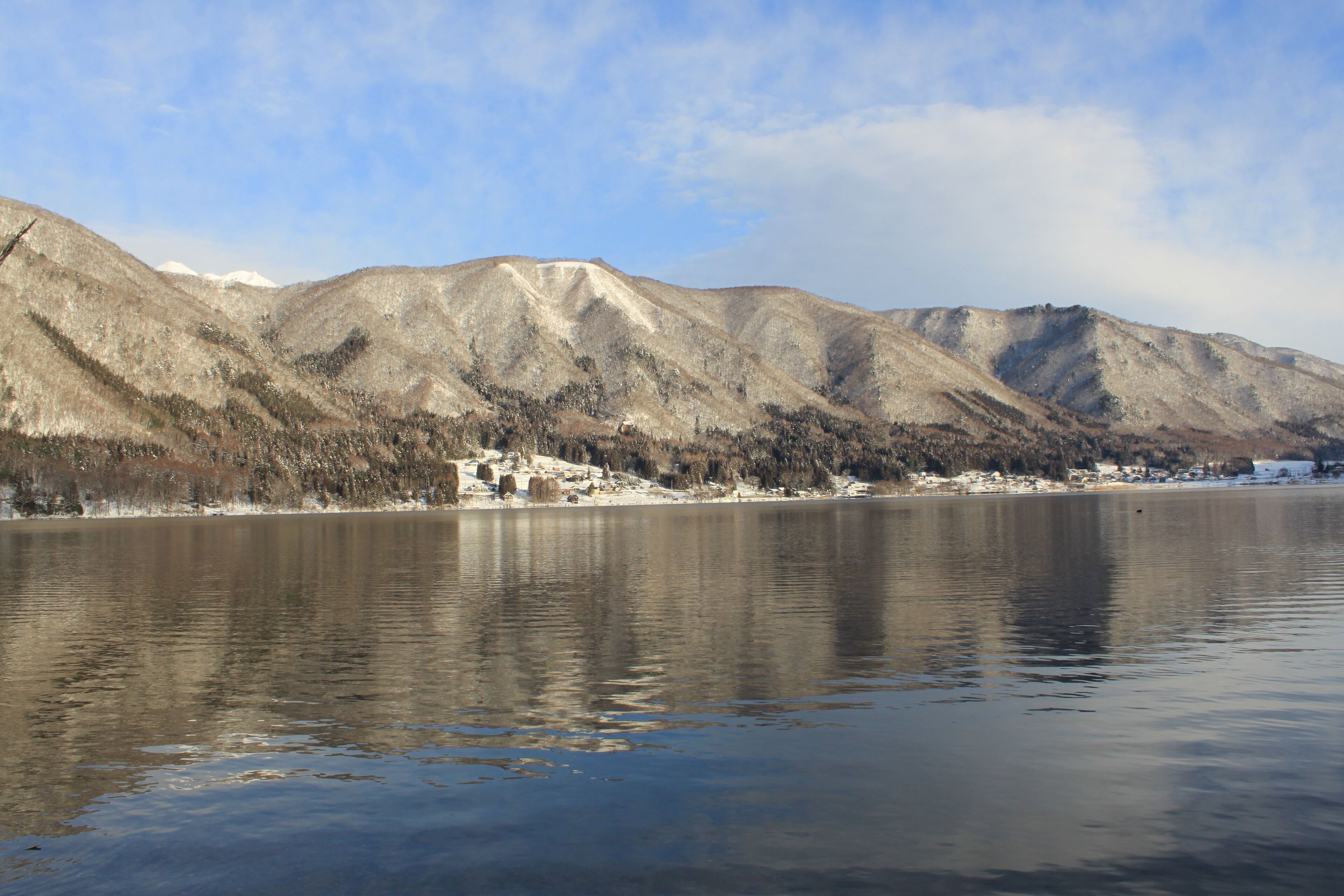 A calm lake with snow-capped mountains in the background and a small settlement on the shore.