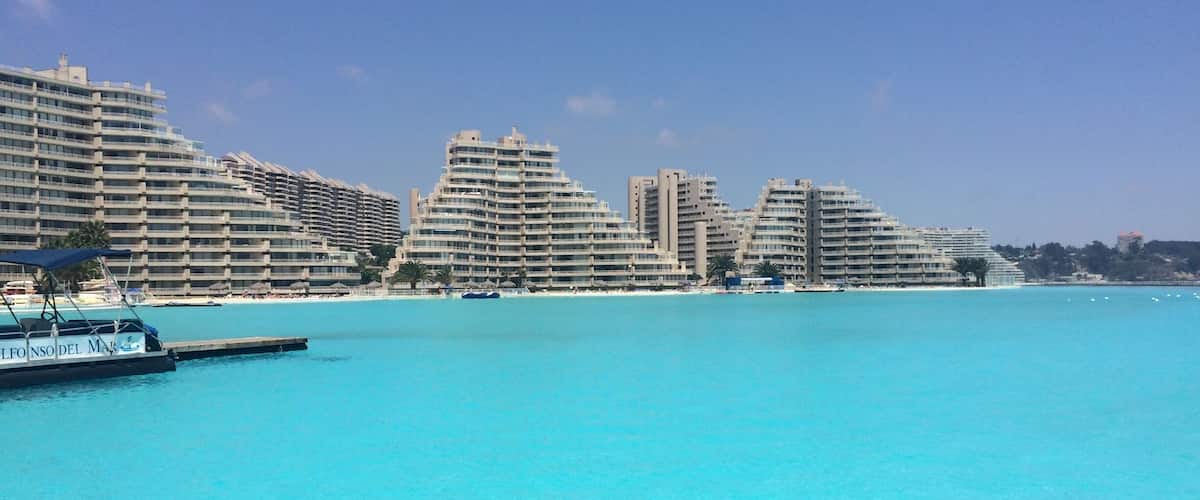 A coastal cityscape with modern high-rise buildings and a clear blue sea.
