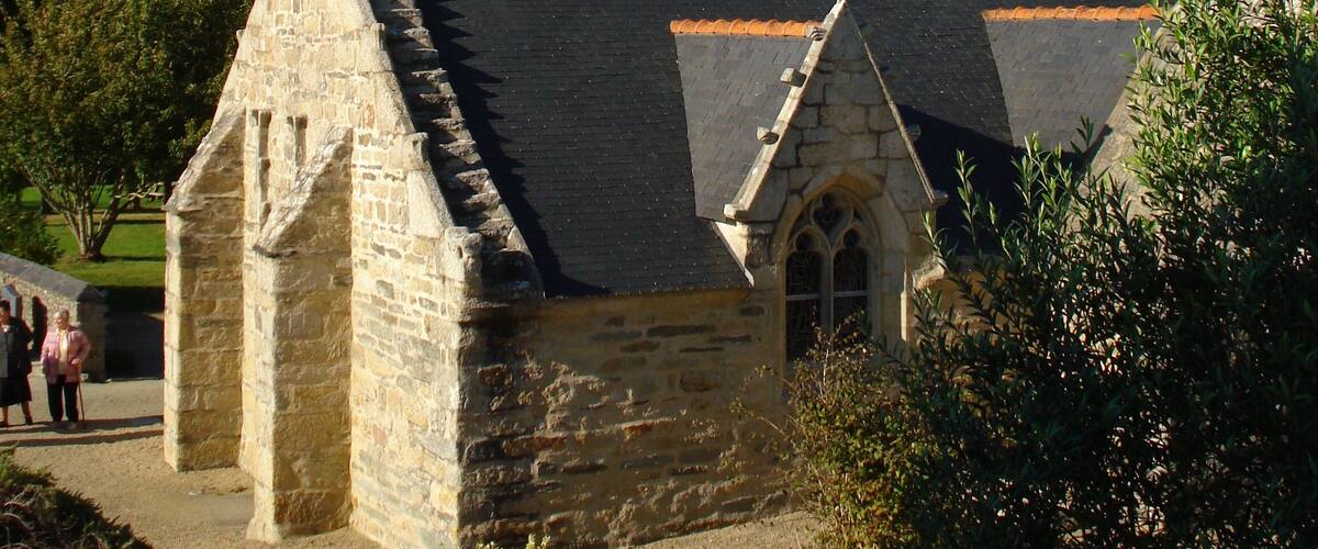 A stone church with a bell tower and a steeple, surrounded by trees and a clear sky.