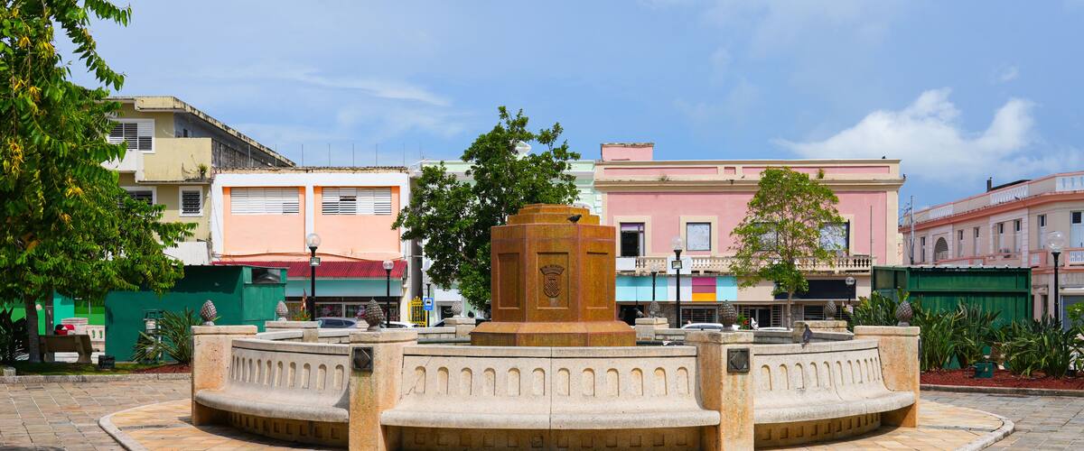 A roundabout with a central monument, surrounded by a paved plaza, with buildings in the background.