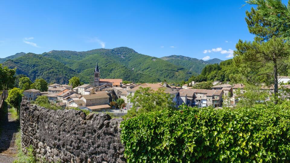 A village with stone buildings, a church with a tower, and green hills in the background.