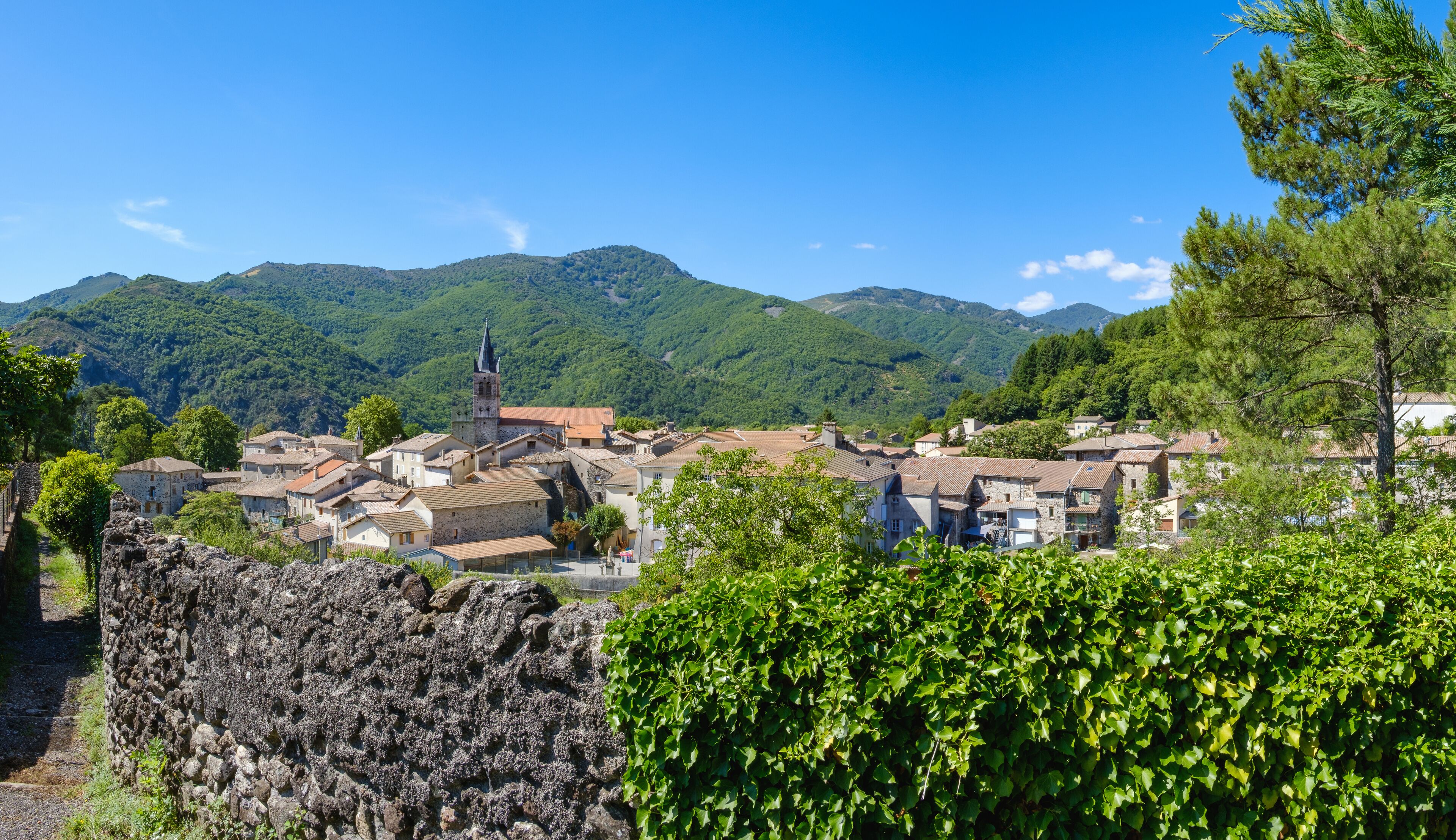 A village with stone buildings, a church with a tower, and green hills in the background.