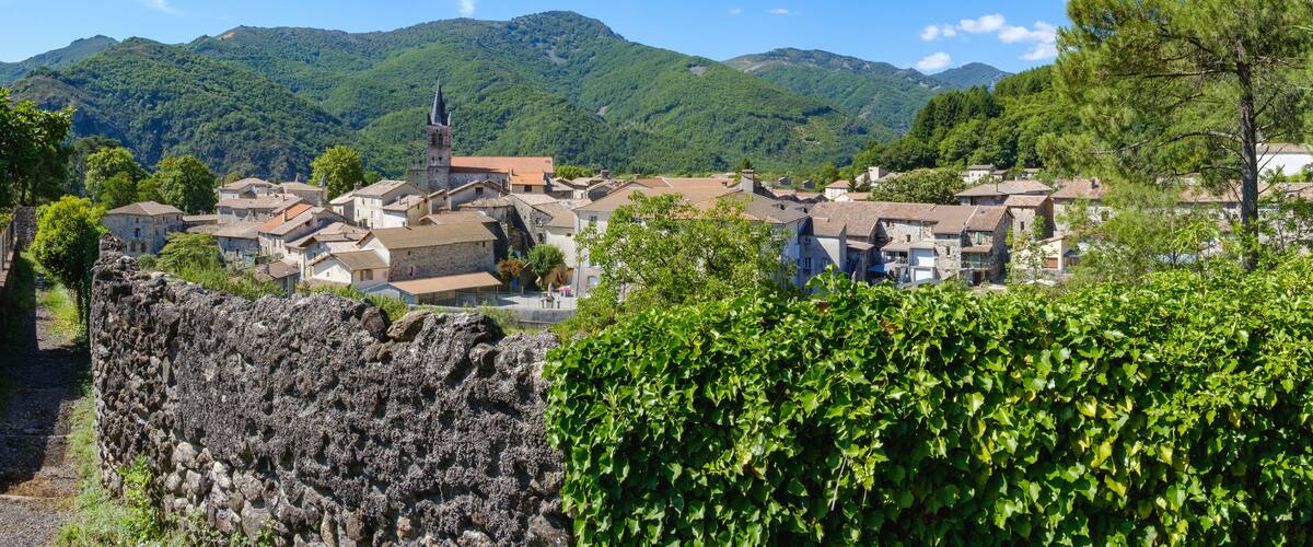 A village with stone buildings, a church with a tower, and green hills in the background.