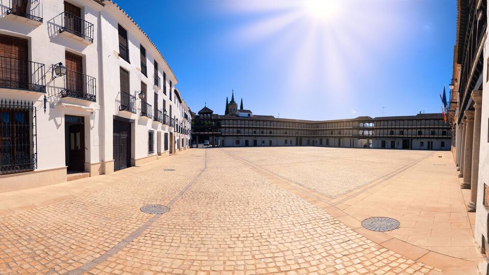 A cobblestone plaza with historic buildings, a church, and a clear blue sky.