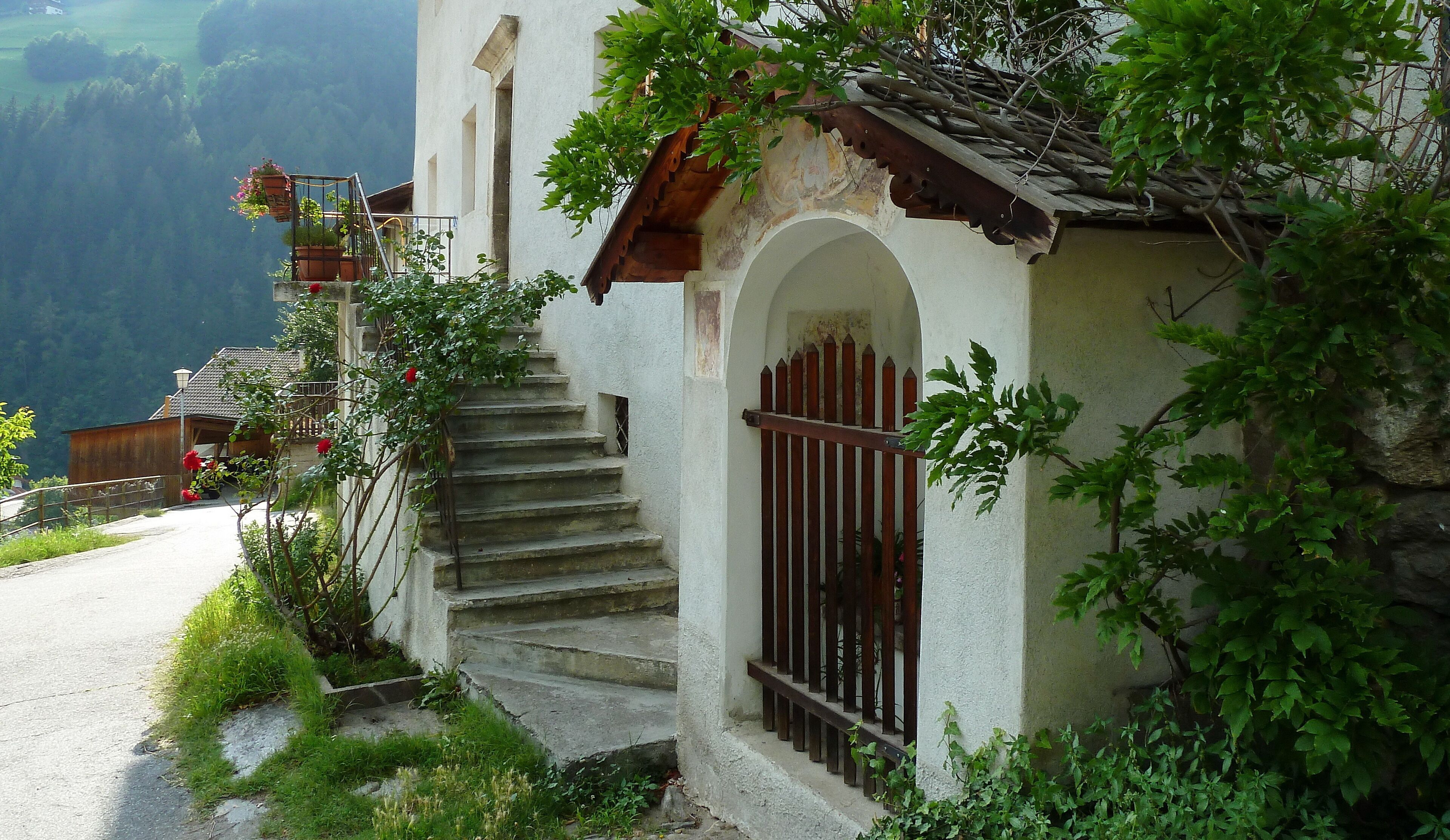 A rustic stone staircase leading to a white building with a wooden roof and a metal gate.
