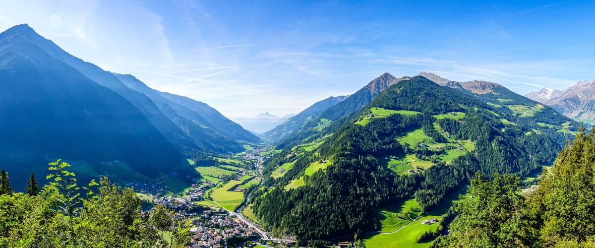 A mountainous landscape with a valley, green fields, and a small town.