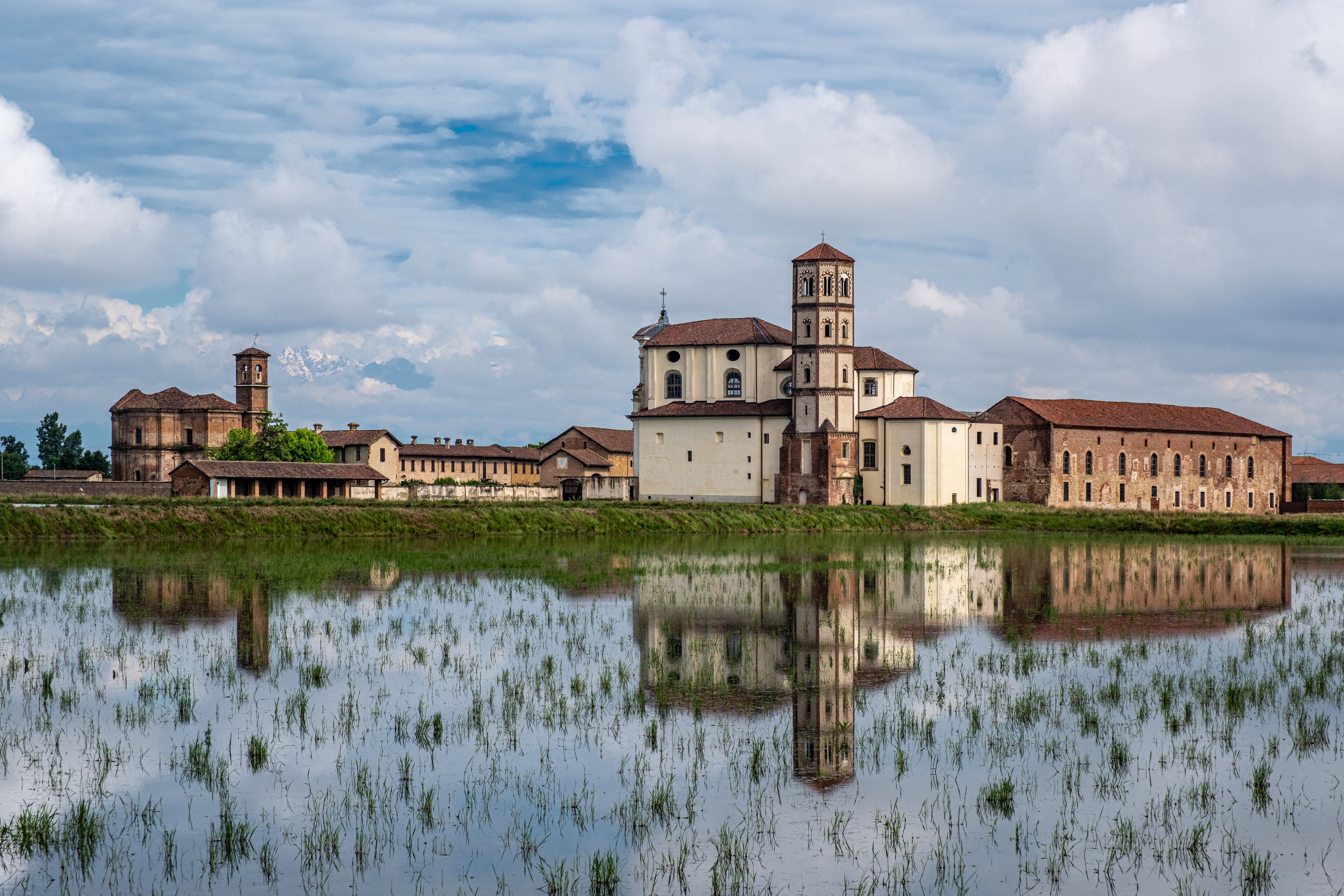 A historic building complex with a central tower and a large body of water in the foreground.