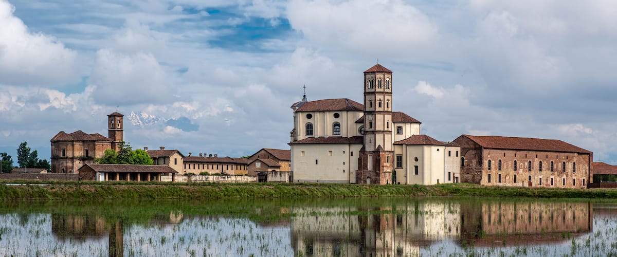 A historic building complex with a central tower and a large body of water in the foreground.