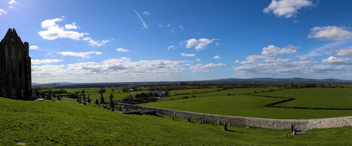 A historic castle, green fields, stone walls, and distant mountains.