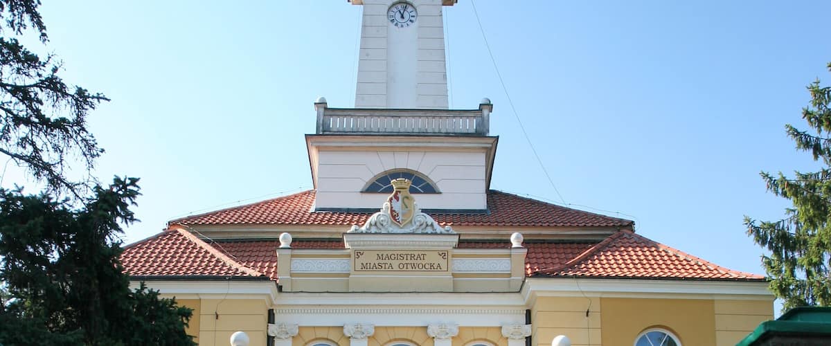 A historic building with a clock tower, a grand entrance with steps, and a green gate.